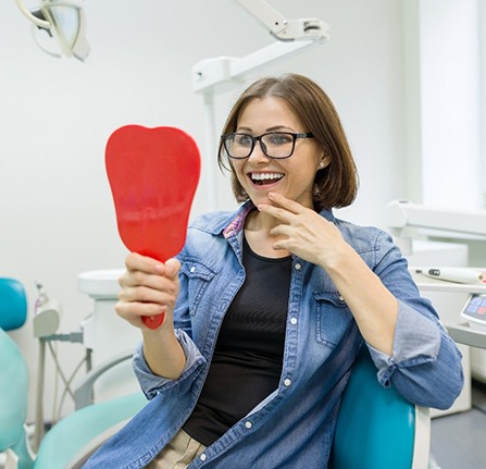 Woman in dental chair looking in the mirror after all on four dental implants