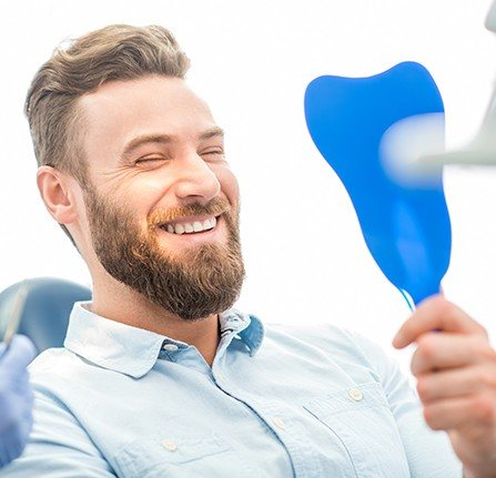 Man with metal free dental crowns looking at smile in mirror