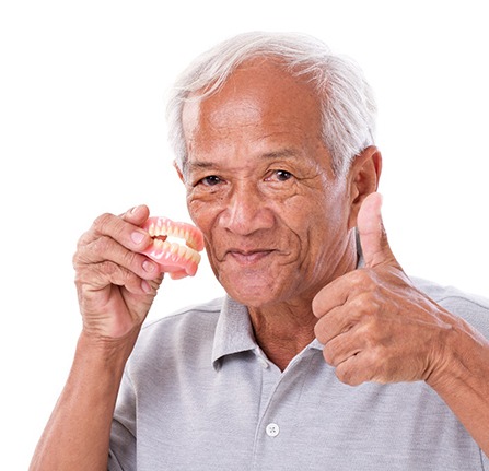 Man holding his dentures and giving a thumbs up