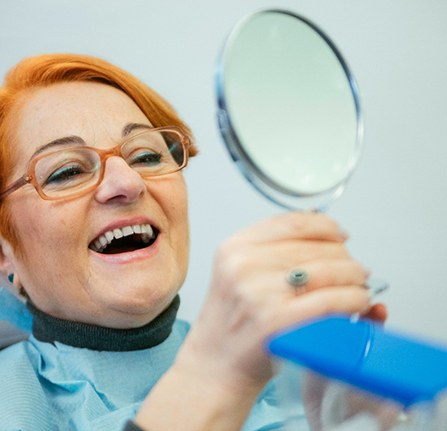 An older woman looking at her dentures in a hand mirror