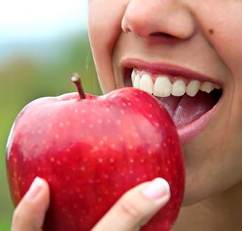 Closeup of patient eating an apple to prevent dental emergencies in Mt. Pleasant