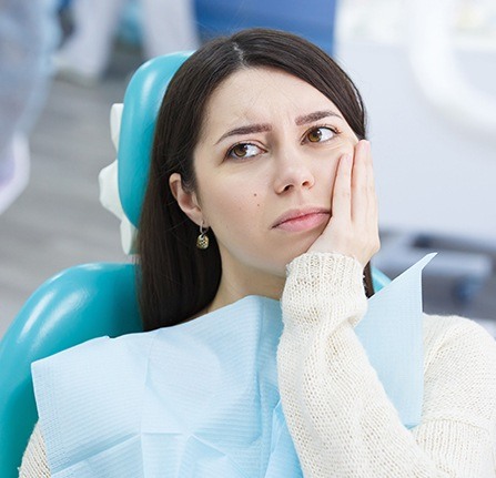 Woman in dental chair holding cheek in pain before tooth extractions