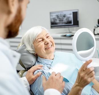 patient with dental implants admiring her new teeth in a mirror
