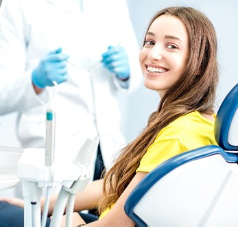 Woman in yellow shirt smiling while sitting in dentist's chair