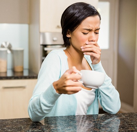 person drinking a cup of coffee and experiencing dental sensitivity