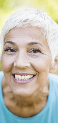 Older woman outdoors smiling after tooth replacement with dental implants