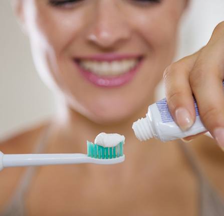 woman putting toothpaste on an electric toothbrush 