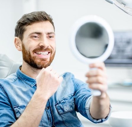 man admiring the results of his teeth whitening treatment in a mirror 