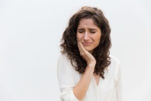 Woman with brown hair in white shirt holding her hand to her face in pain